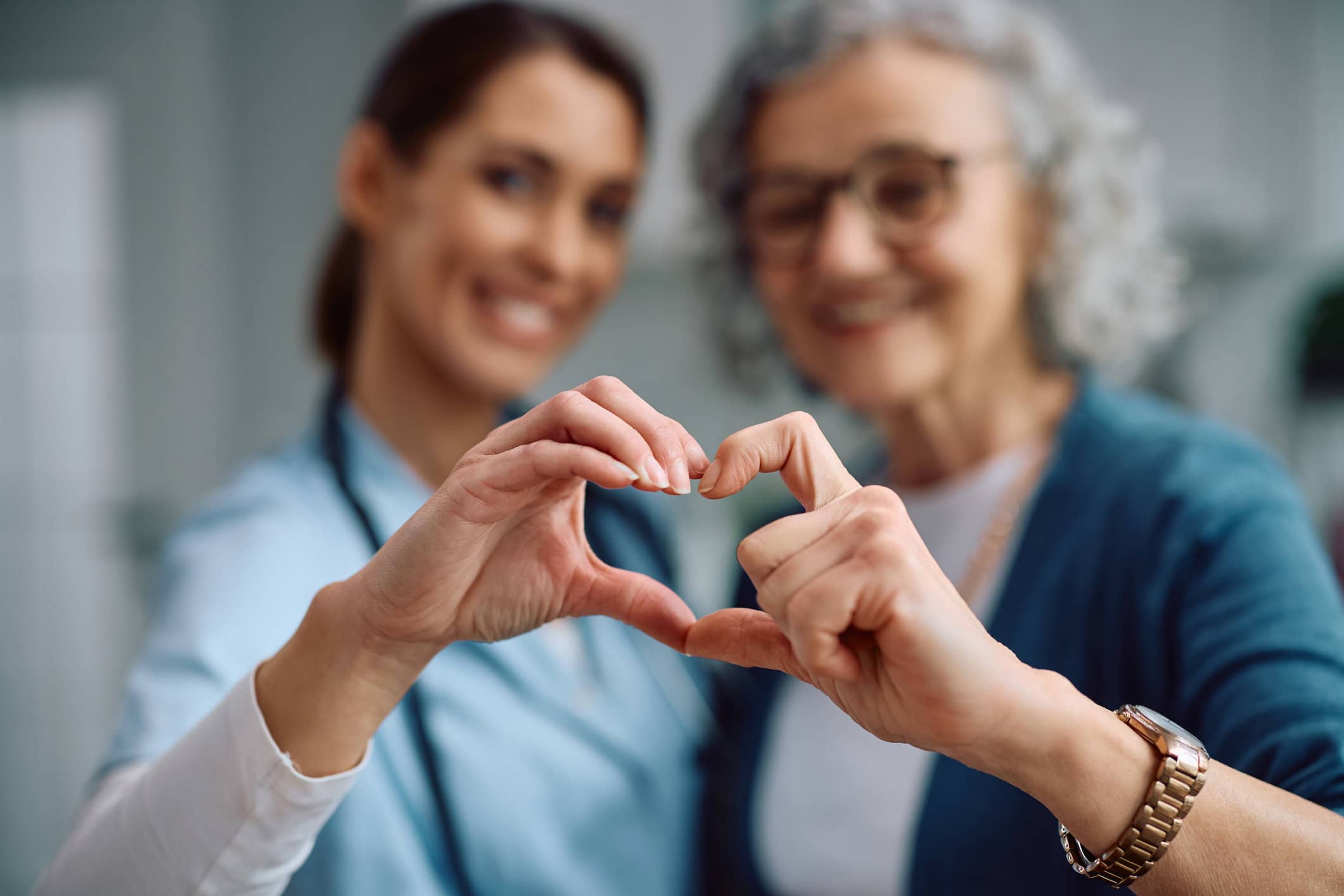 nurse and senior woman making heart shape with hands.